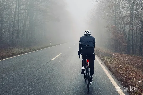 高清摄影 穿着黑色夹克的男人在雾天的道路上骑自行车。