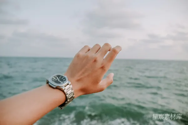 一个手戴手表的人站在海边