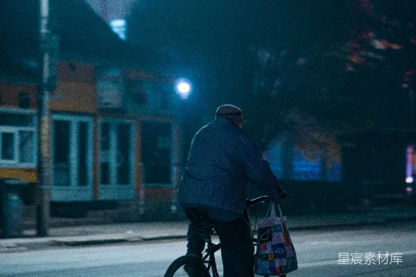 高清摄影 一个穿着灰色夹克的男人在夜晚的道路上骑自行车。