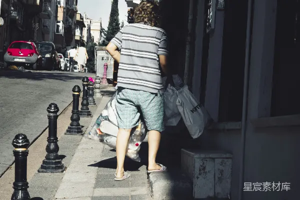 高清摄影 一个人在人行道上走着，手里拿着一个袋子。