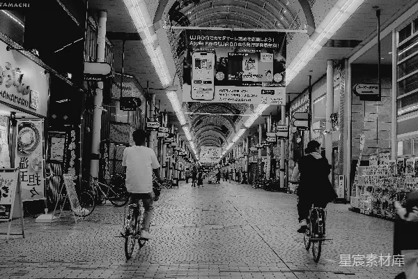 高清摄影 两人在长长的、有遮盖的市场通道上骑自行车。