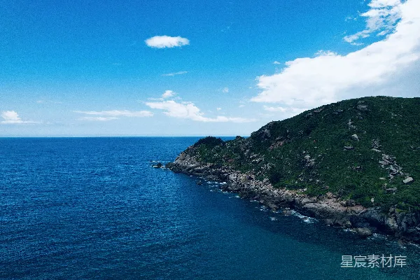 绿色和黑色的山峦位于蓝色的大海之旁，在蔚蓝的天空下在白天。
