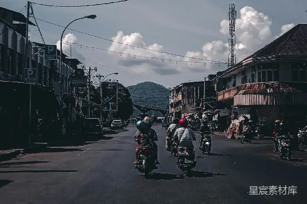 高清摄影 人们在道路附近骑摩托车，旁边是人和建筑物。