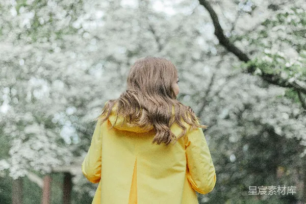 黄色风衣的女人在树木边站立，白天。