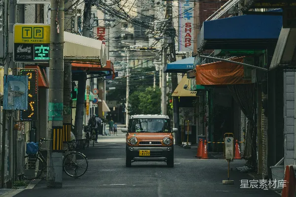 橙色小轿车在一条狭窄的城市街道上行驶。