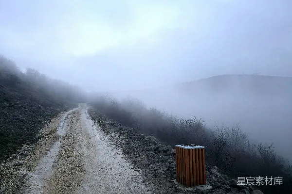 一条尘土路蜿蜒穿过一片雾气缭绕的山地景观。