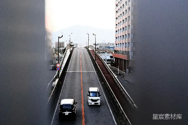 高清摄影 两辆汽车在高楼大厦旁边的城市街道上行驶。