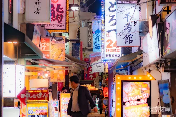 高清摄影 一个男人在一条充满活力、霓虹灯闪烁的日本街道上行走。
