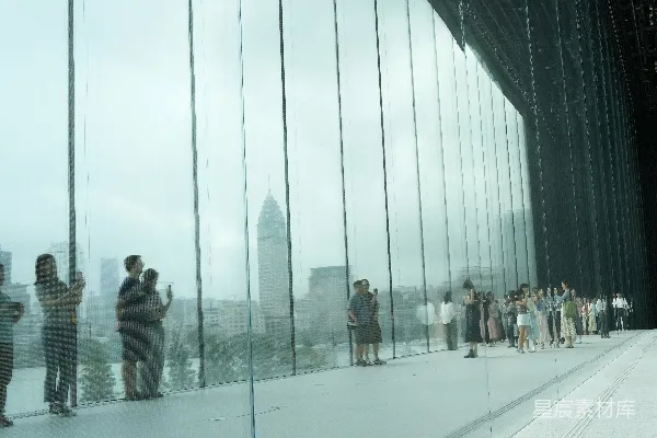 人们透过一大块玻璃墙看向城市。