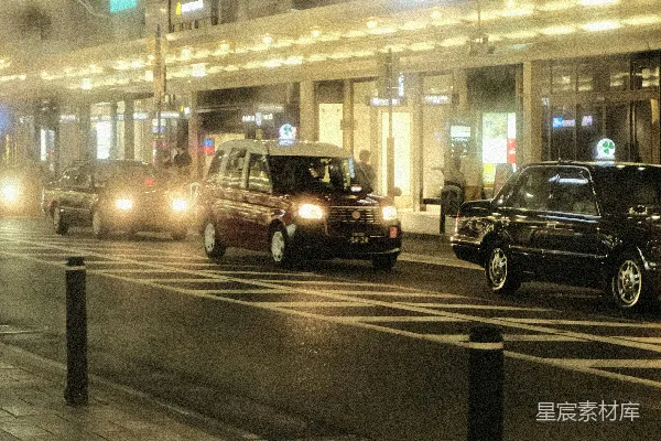 高清摄影 一排汽车沿着街道行驶，旁边有一栋高楼。
