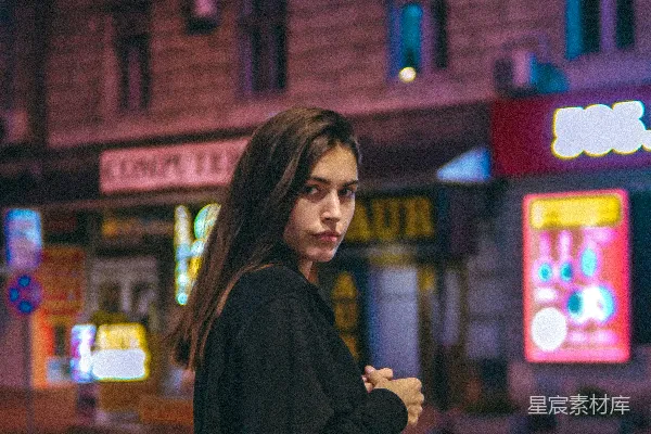 黑外套的女人站在红建筑附近的一个夜晚。