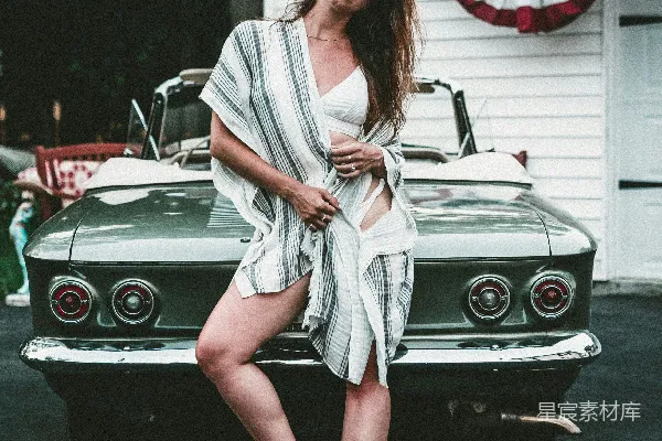 女人站在车旁靠在灰色的汽车上，户外场景