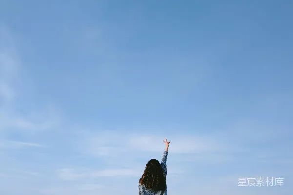 高清摄影 穿着灰色上衣的女人在蓝天背景下做出和平手势。