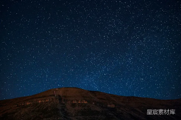 一片浩瀚的星空映衬在一座黑暗且轮廓分明的小山之上。