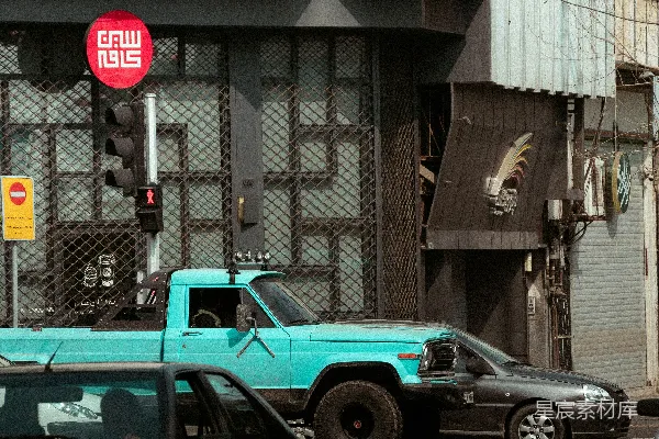 一辆蓝色的卡车在一条街上行驶，旁边是一栋高大的建筑。