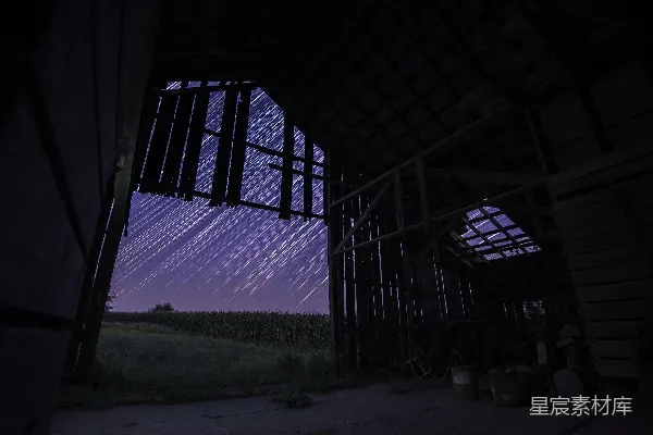 夜晚，长时间曝光下的星空映衬在一座棕色木屋上方。