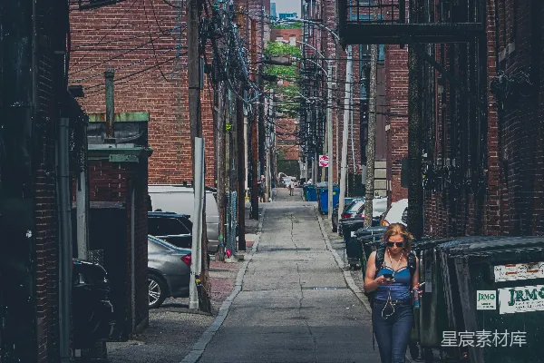 一个女人走在一排高建筑物旁边的小路上
