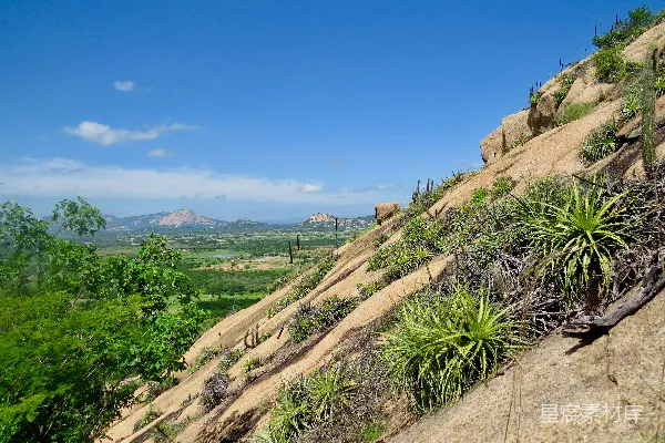 绿色草地在棕色岩石山下，在蓝天之下，白天时