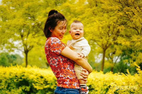 妇女抱着一个笑着的婴儿靠近树木
