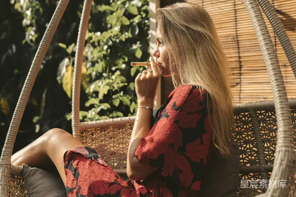红黑花卉连衣裙的女人坐在棕色的藤编扶手椅上。