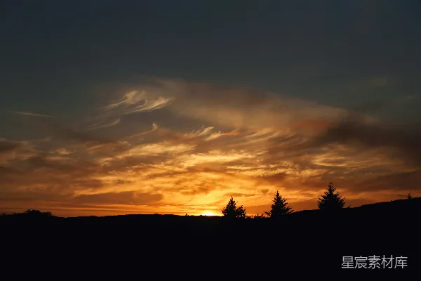 夕阳映照在一片黑暗的轮廓景观上，背景为树木。