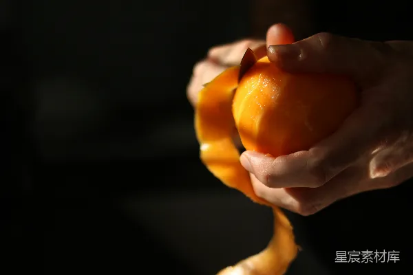 高清摄影 双手在温暖的光线下剥开一个新鲜的橙子。