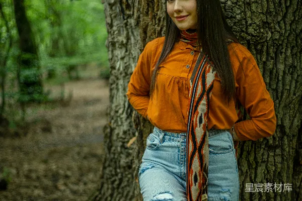 高清摄影 一个女人站在森林里的一棵树旁边。