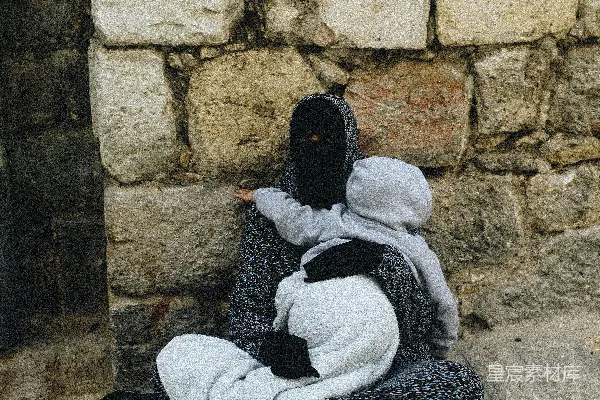 女人坐在地上靠着墙抱着婴儿。