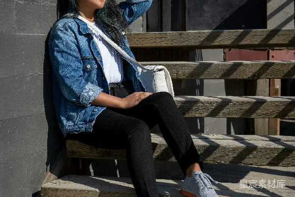 高清摄影 穿着蓝色夹克和黑色裤子的女人坐在棕色木制长椅上。