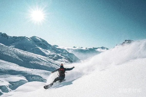 一个男人在覆盖着积雪的山坡侧边骑着单板滑雪下降。
