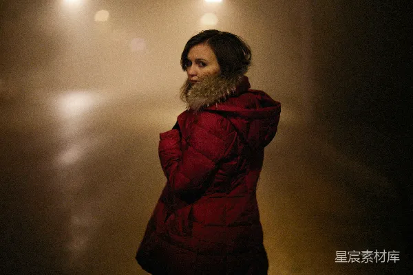 一个穿红色外套的女人站在一间黑暗的房间中
