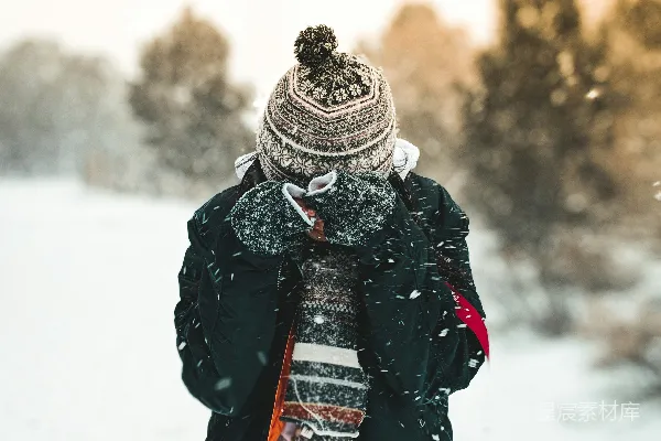 戴着贝雷帽和黑色连帽外套的人站在覆盖着雪的草地上站立。