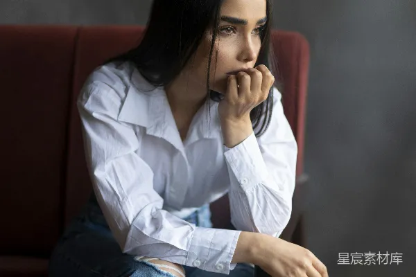 白衬衫着装的女士坐在红色沙发上，穿着蓝色直筒牛仔裤。
