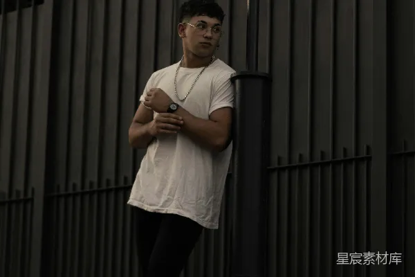 白tee衫和黑色裤子的男人站在灰钢门旁边挺直身子