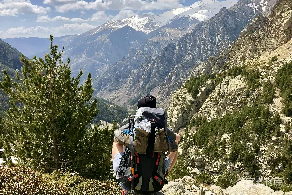 男人坐在悬崖上，在白天观赏远处的山和树。