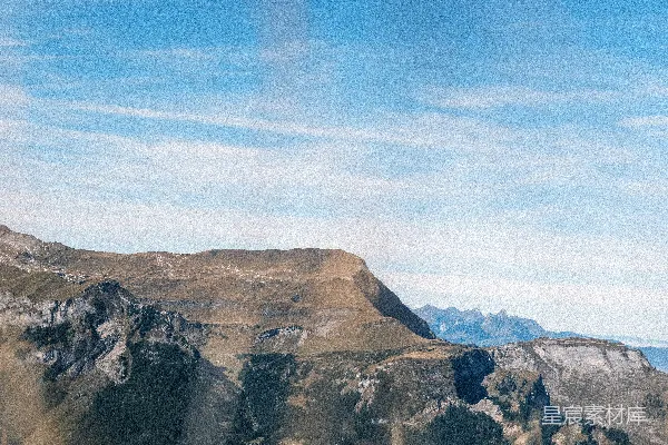 foreground金色草丛，远处有岩石山脉和蓝天。