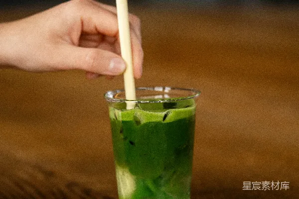 一只手拿着牙签，对着一杯绿色的饮料。