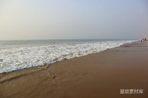 几个行人沿着海滩走，在海边附近