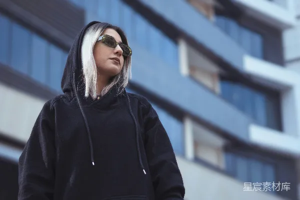 一位白发女子戴着太阳镜站在建筑物前。
