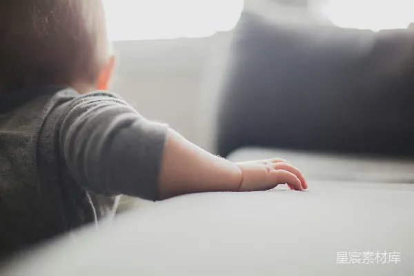 蹒跚学步的孩子穿着灰色上衣抓住沙发