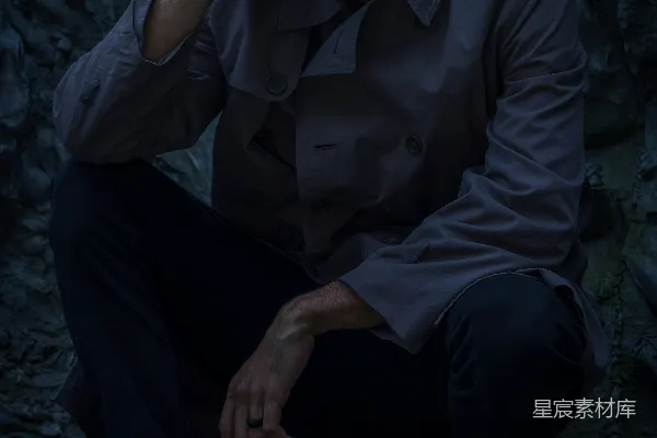 一个男人坐在一块岩石上，手放在头上。