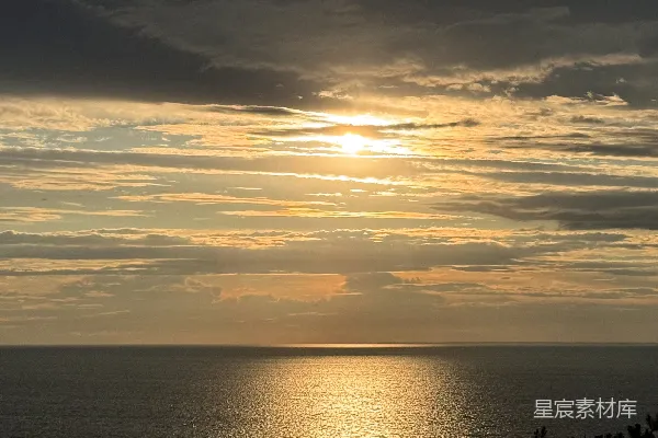金色的夕阳映照在平静的海洋上，云朵缭绕。