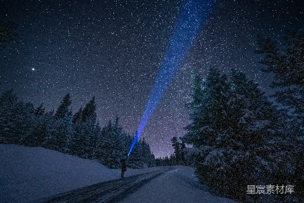 一个人站在覆有白雪的道路旁，在满天星斗的天空下。