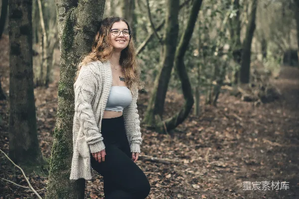 高清摄影 一个女人站在森林里的一棵树旁。
