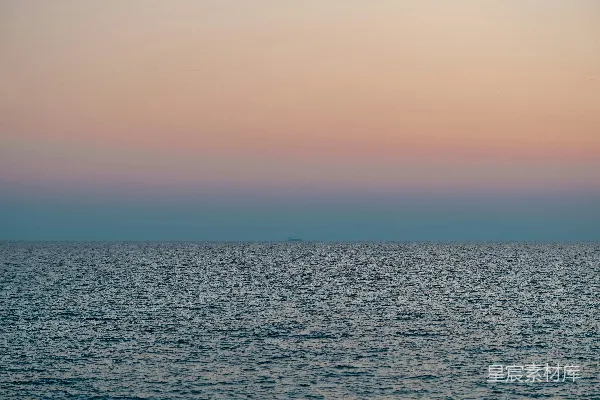 在浅粉色的夕阳天空下平息波涛的大海。