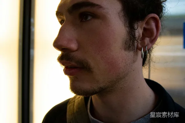 一个留有络腮胡子和耳环的男人站在窗户前。