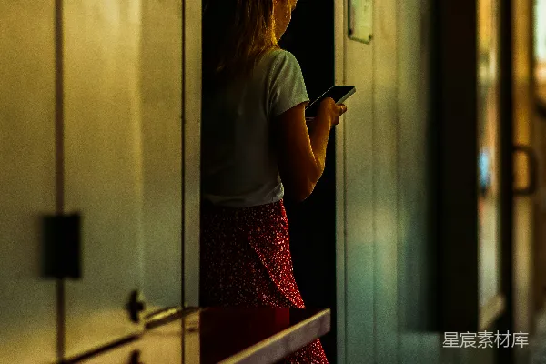 女士在昏暗的走廊里盯着手机看。