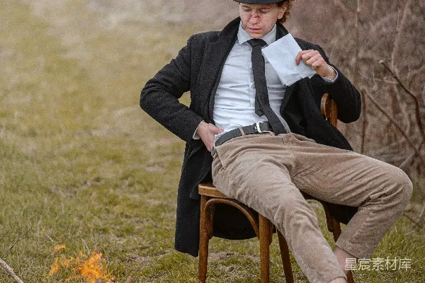 一个男人坐在一把椅子旁边，旁边是一堆火。