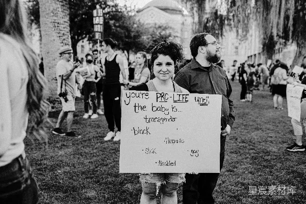 一名妇女在一群人的面前举着一块牌子。