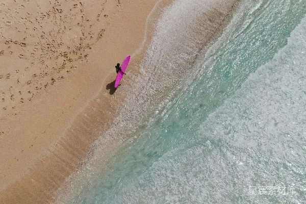 海滩上一个人拿着冲浪板的空中视角